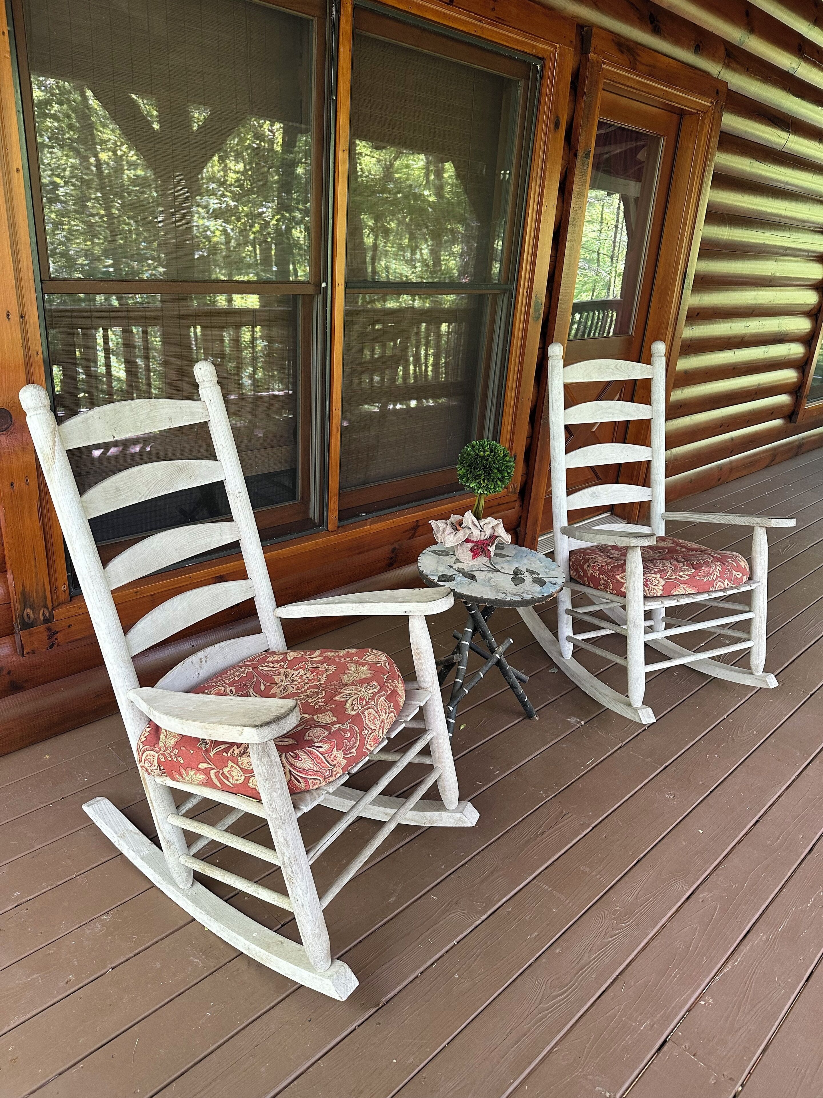 A wooden rocking chair with a floral cushion and another chair with a patterned cushion on a wooden deck.