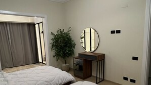 A bedroom with two beds, a mirror, a potted plant, and a ceiling light.