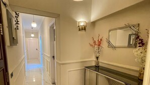 A hallway with a marble floor, a wooden ceiling light, a wall-mounted mirror, and a console table with a vase of flowers.