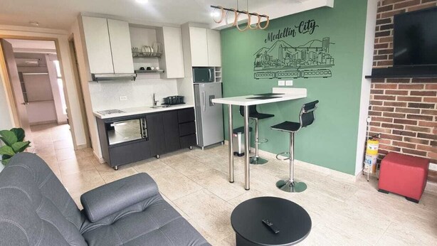 A compact living space with a kitchenette, a dining area, a sofa, and a TV mounted on a brick wall. - Cold AC K Fast WiFi Medellin Paradise (Medellín)