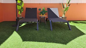 Due poltrone, un tavolino con un drink e piante in vaso in un’area relax esterna con erba sintetica e un muro in lamiera ondulata.