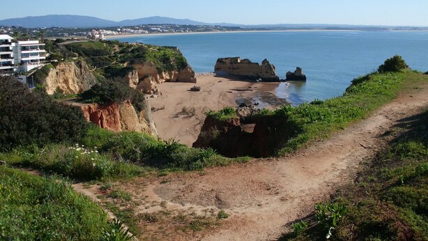Un sentiero costiero che conduce a una spiaggia con affioramenti rocciosi e una vista limpida sul mare.