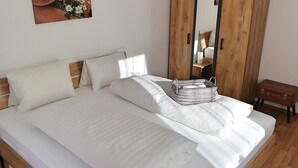 A neatly made bed with white linens and pillows, a wooden headboard, a wooden wardrobe with a mirror, and a small wooden bench. - Vacation apartment DIRECTLY at the lift in the Ski Amadé - Haus Daniel Schartner Kleinarl (Kleinarl)
