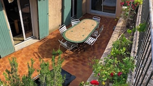 Un patio exterior con una mesa y sillas, una puerta corrediza de vidrio y un jardín con flores.