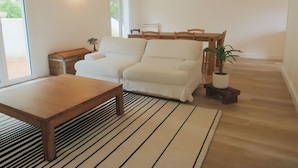 Una sala de estar con un sofá, una mesa de centro de madera, un tapete a rayas, una mesita auxiliar de madera y una planta en maceta.