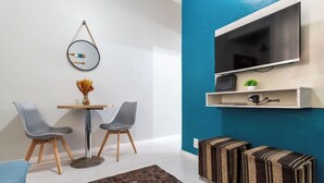 Una sala de estar moderna con una pared azul de acento, una mesa redonda con dos sillas, un televisor montado en la pared y un estante pequeño con una planta y una tetera.