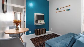 Una sala moderna con una pared azul de acento, un televisor de pantalla plana, una mesa de comedor con sillas y un sofá azul.
