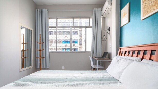 Habitación de hotel con una cama, un escritorio con una computadora portátil, una silla y vistas a edificios a través de la ventana.