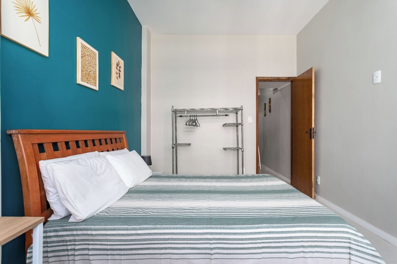 A bedroom with a wooden bed, a metal drying rack, and teal walls.