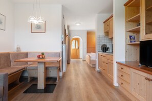A modern kitchen with wooden cabinets, a dining area with a bench, and a hallway leading to a door.
