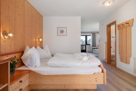 A wooden bed with white bedding, a bedside table with a vase of flowers, and a wooden wardrobe with a mirror.