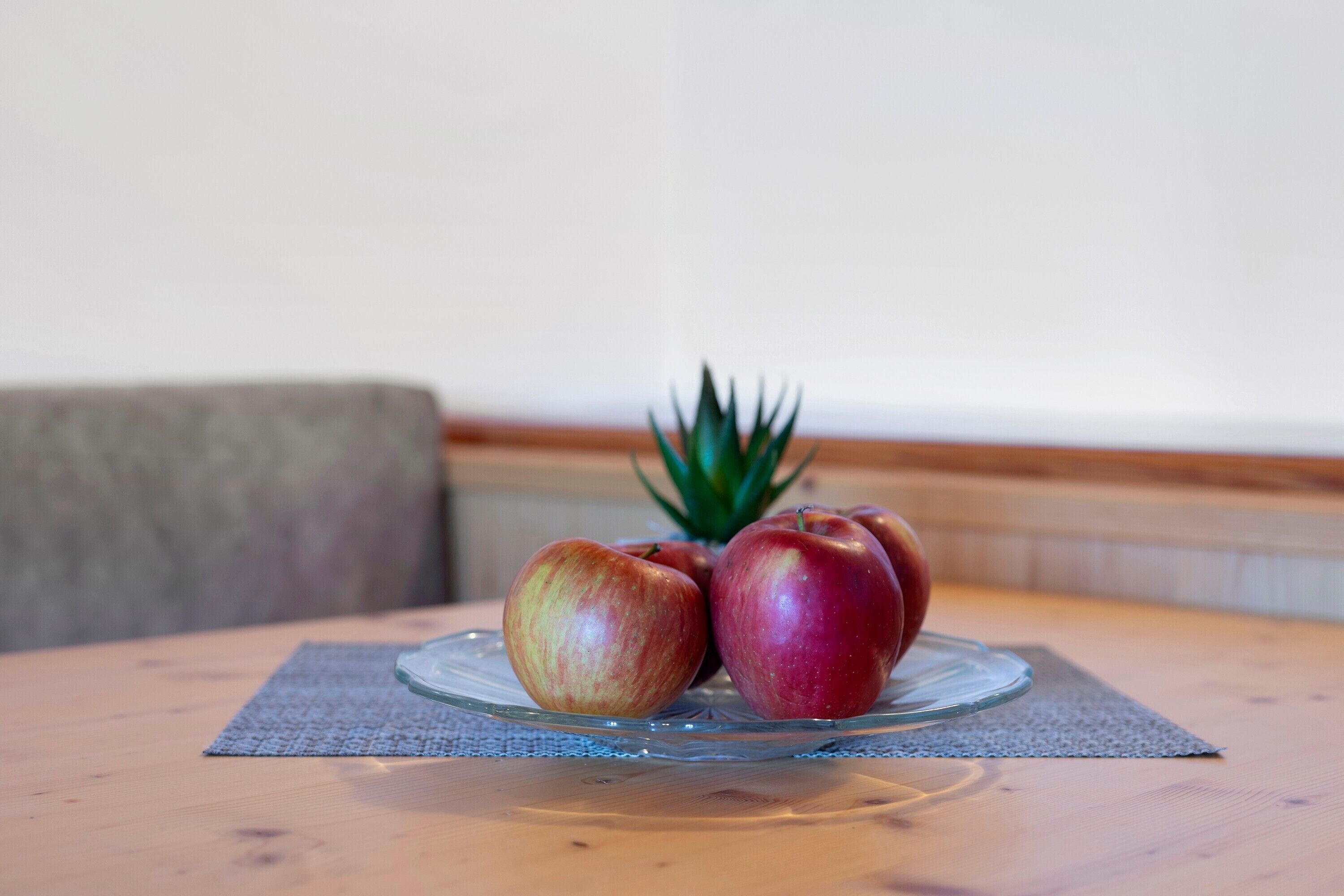 A table with a glass plate holding two apples and a pineapple.