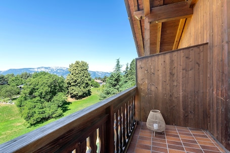 A wooden balcony with a view of a green landscape and mountains.