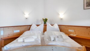 Una cama doble con ropa blanca, dos mesitas de noche, una planta pequeña y luces fijadas a la pared.
