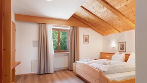 Un dormitorio con techo de madera, una ventana con cortinas, una cama con sábanas blancas y un radiador.