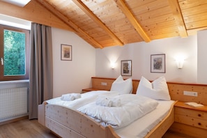 Ein Zimmer mit Holzbalken, einem Bett, Nachttischen und einem Fenster mit Vorhängen.