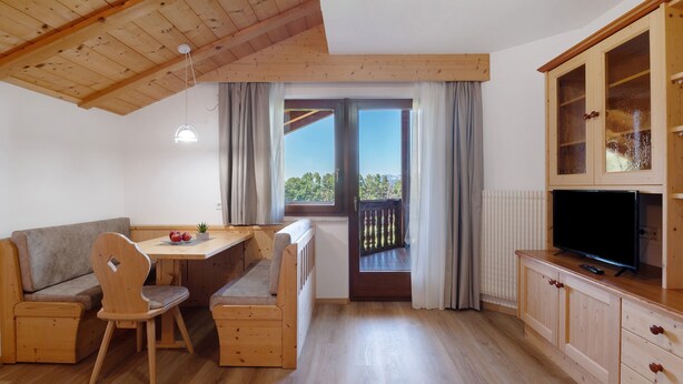 Una habitación acogedora con techo de madera, una mesa de comedor con sillas, un sofá, un televisor sobre un mueble de madera y una ventana con vistas.