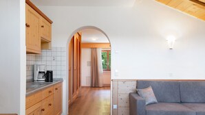 Una cocina con armarios de madera, cafetera y comedor con sofá y cortinas.
