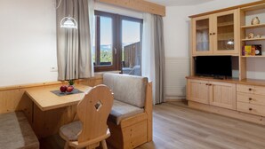 Una habitación acogedora con un escritorio de madera, una silla con cojín, un televisor y un armario con estantes.