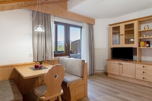 Ein gemütliches Zimmer mit einem Holztisch, einem gepolsterten Sessel, einem Fernseher und einem Schrank mit Regalen.