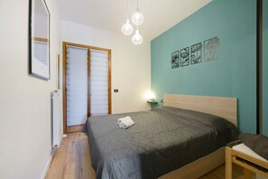 A bedroom with a bed, a nightstand, a wall-mounted lamp, and a door with a window.