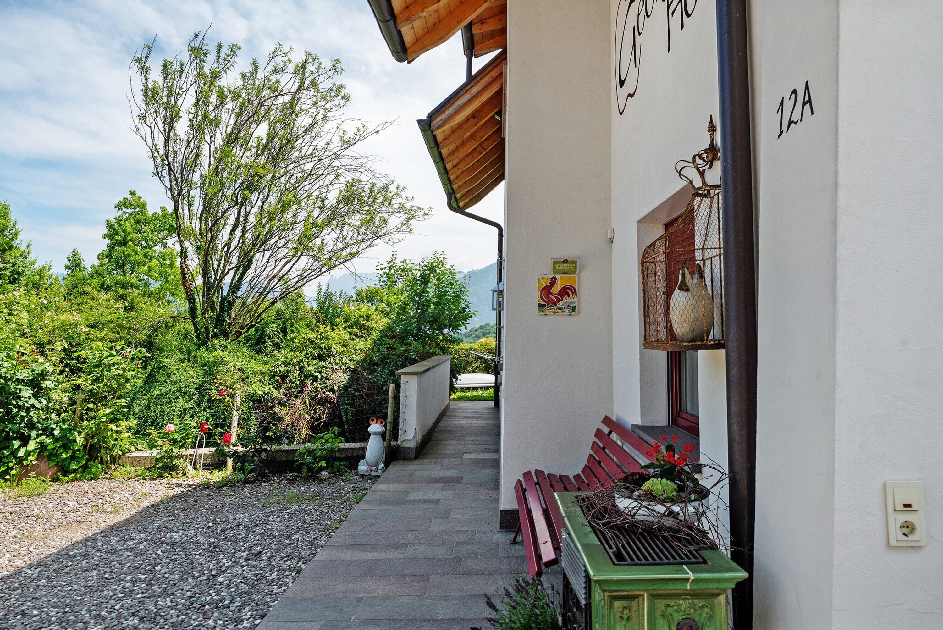 A building with a green bench outside, a rooster decoration, and a number '12A' on the wall.