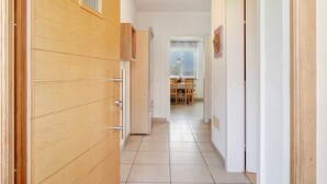 Ein Flur, der in einen Essbereich mit Fenster, Holzschränken und Fliesenboden führt.