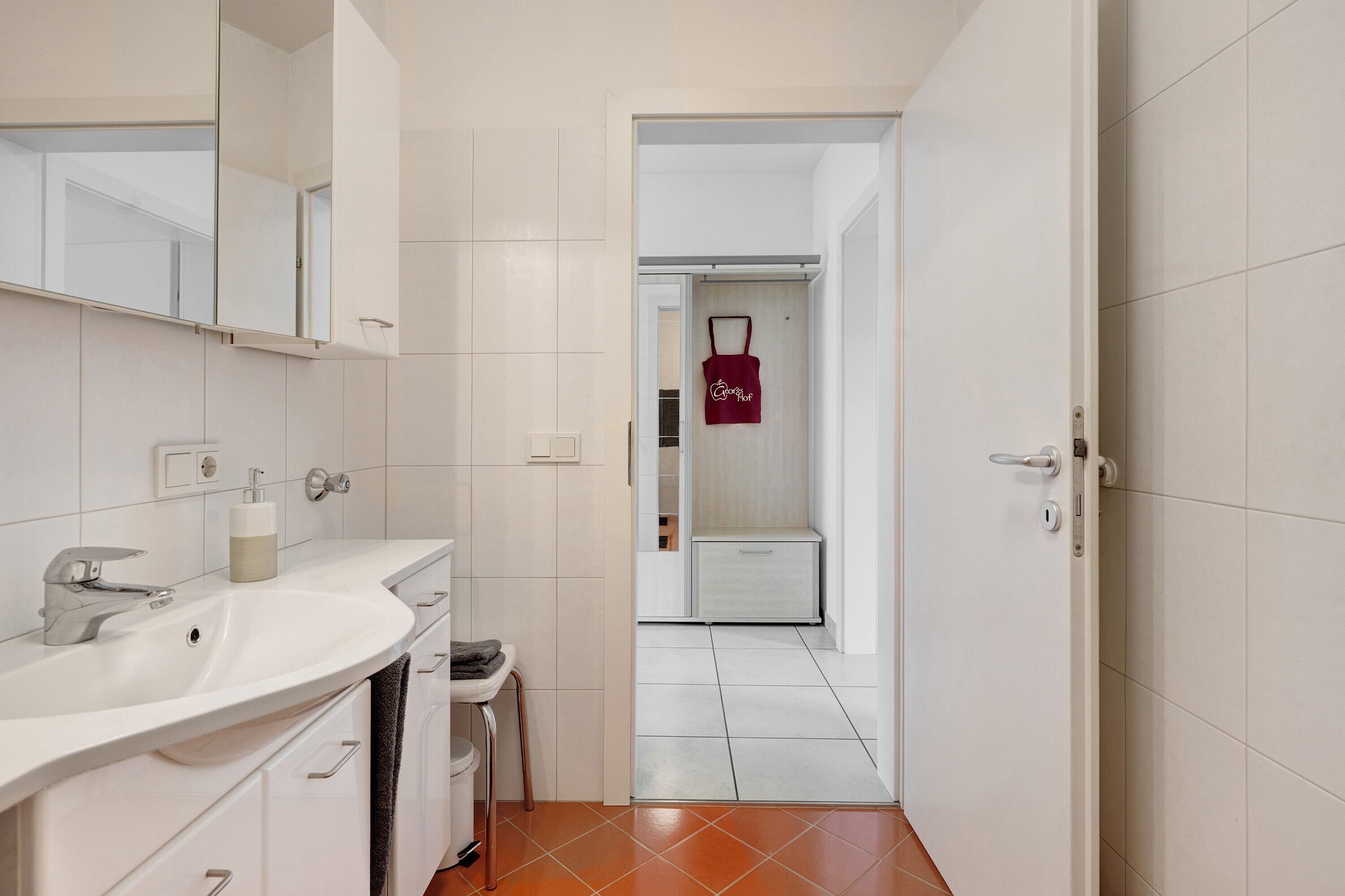 Un baño con lavamanos blanco, espejo y perchero.