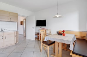 A modern kitchen with wooden cabinets, a dining table with a white tablecloth, and a television mounted on the wall. - Apartment 'Pink Lady' with Mountain View, Shared Terrace and Wi-Fi (Appiano sulla Strada del Vino)