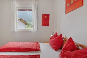 Um quarto com cama, almofadas vermelhas, janela com vista para montanhas e decoração de parede vermelha.