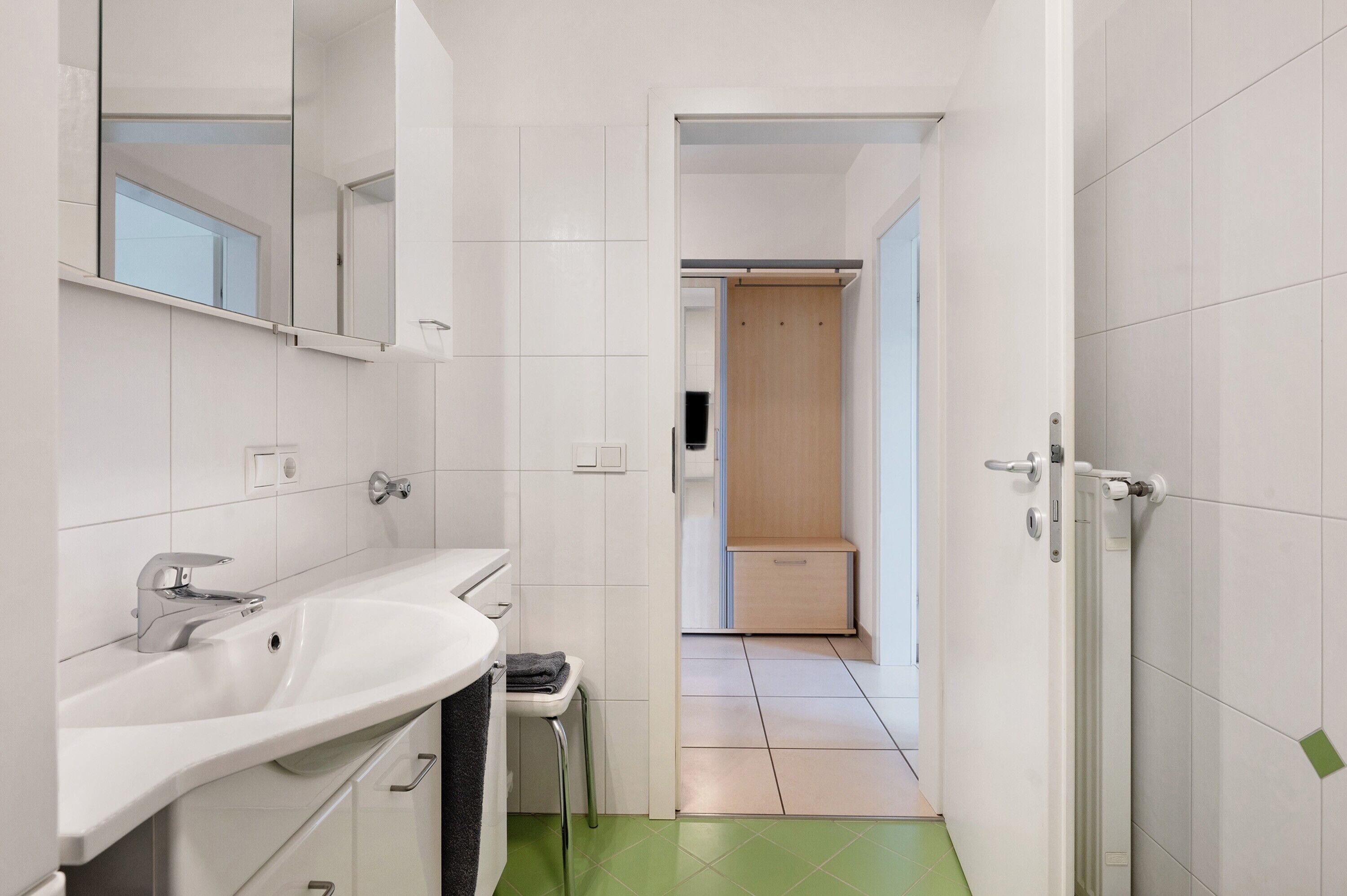 Ein modernes Badezimmer mit einem weißen Waschbecken, einem Spiegel und einem grünen Boden.