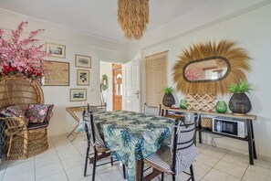 A dining area with a table set for four, surrounded by wicker chairs, a woven chair, and a mirror with a unique frame. - Apartment 'Theodoros  1' with Sea View, Wi-Fi and Air Conditioning (Nikiana)