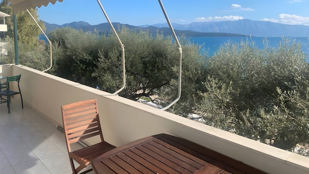 A balcony with a wooden table and chair, overlooking a mountainous landscape and a body of water. - Apartment 'Theodoros  1' with Sea View, Wi-Fi and Air Conditioning (Nikiana)