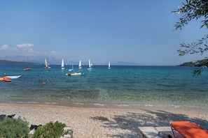 A beach with clear water, boats, and a distant mountain range.