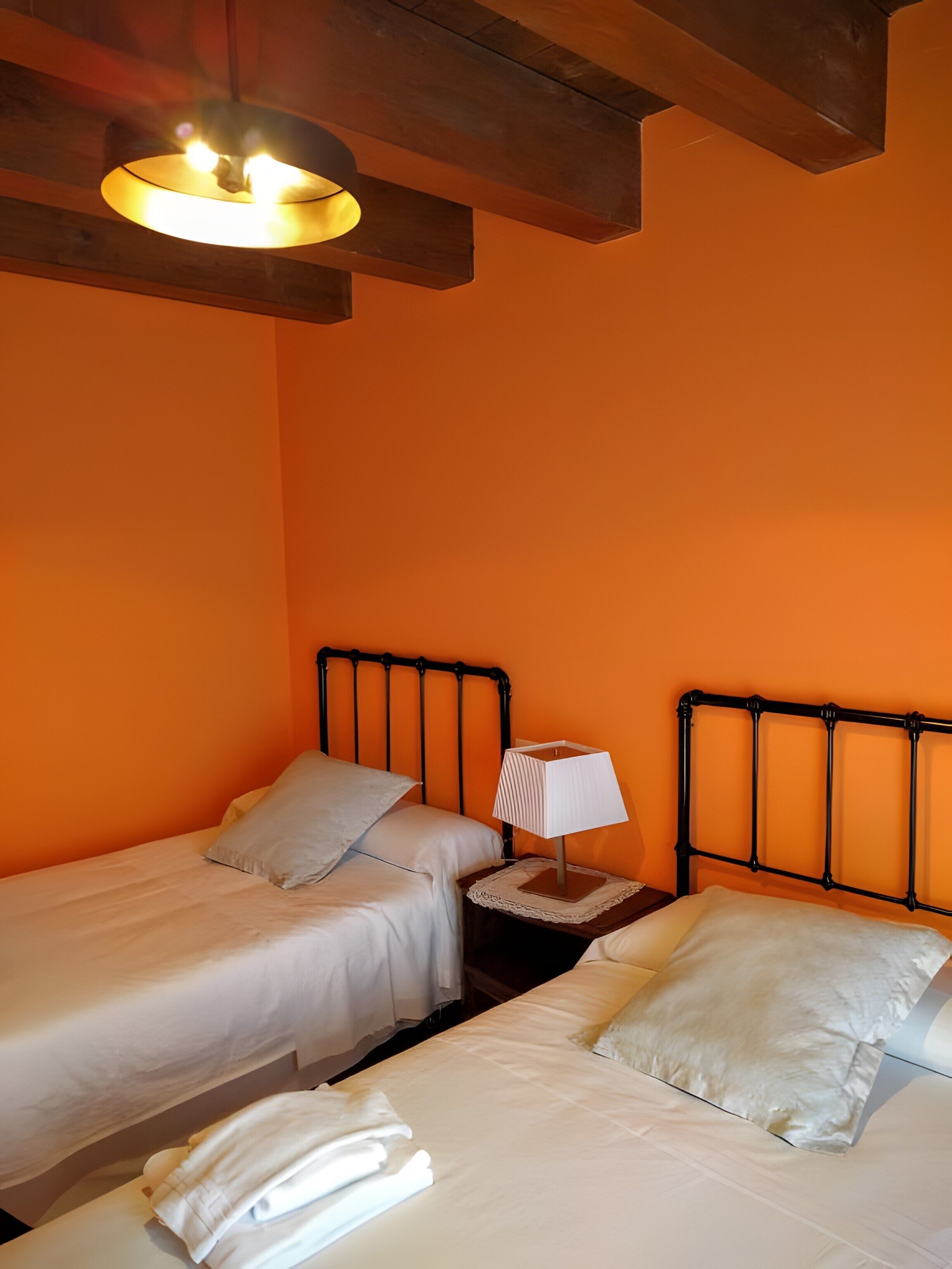 A room with two beds, a nightstand with a lamp, and a ceiling light fixture.