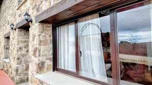 A stone exterior wall with a window featuring a dark frame and sheer curtains.