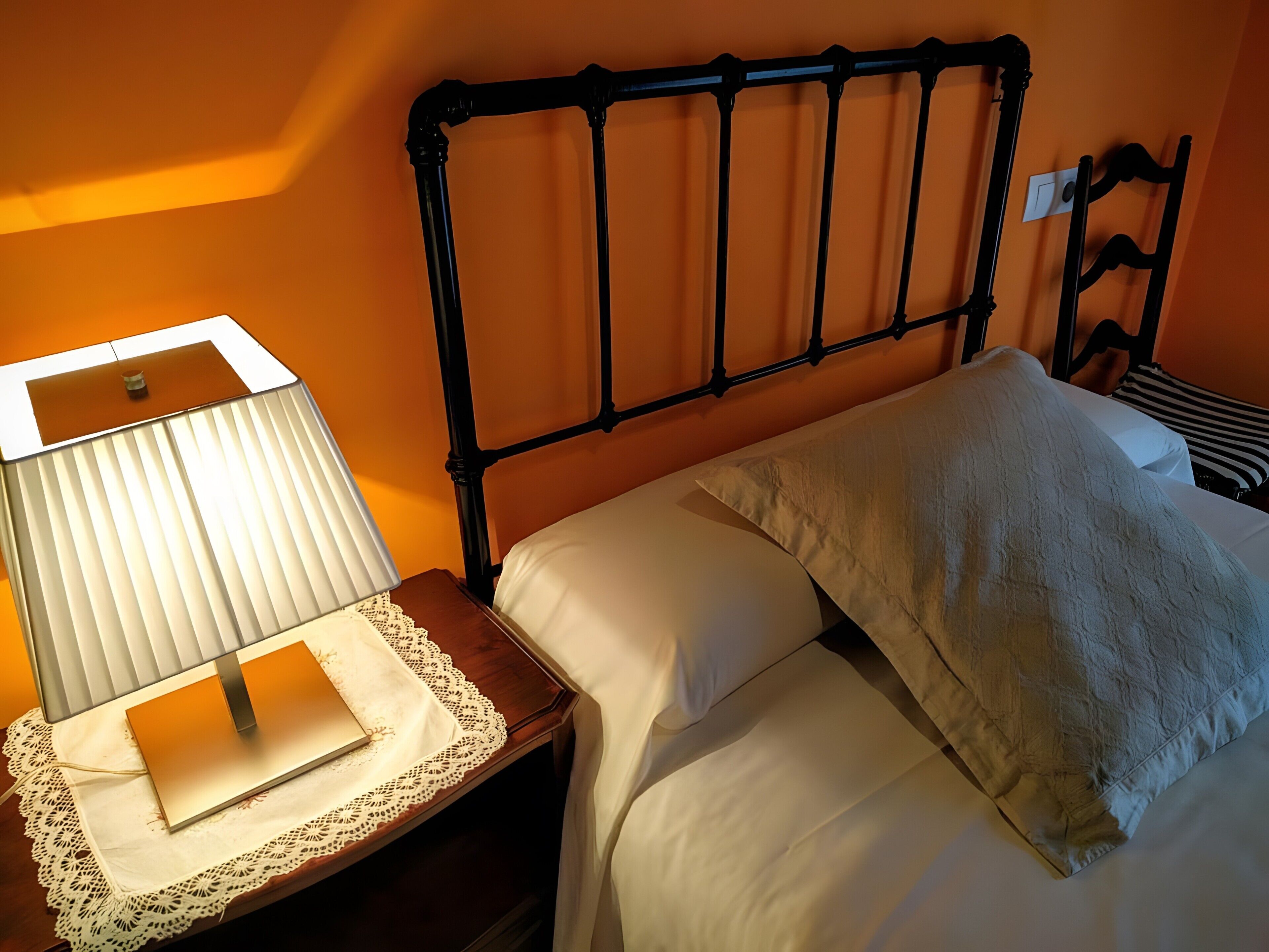 Una cama con sábanas blancas, una mesita de noche con lámpara y un mantel con encaje.