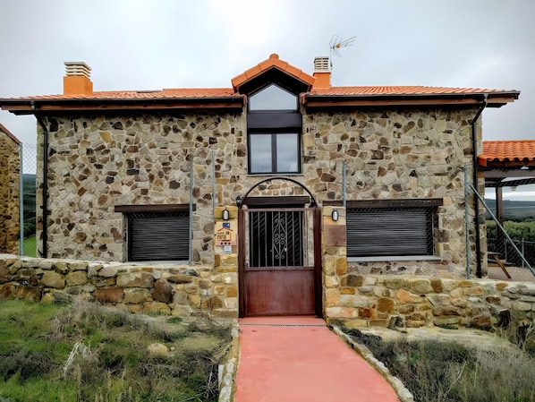 A stone building with a red-tiled roof, a central entrance with a wooden door, and a small window above the door.