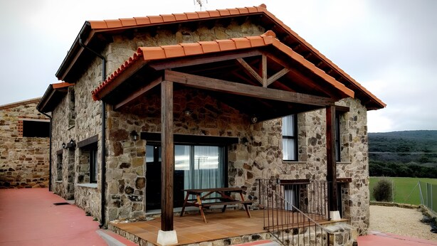 A stone building with a wooden porch, steps leading to the entrance, and a view of the surrounding landscape.