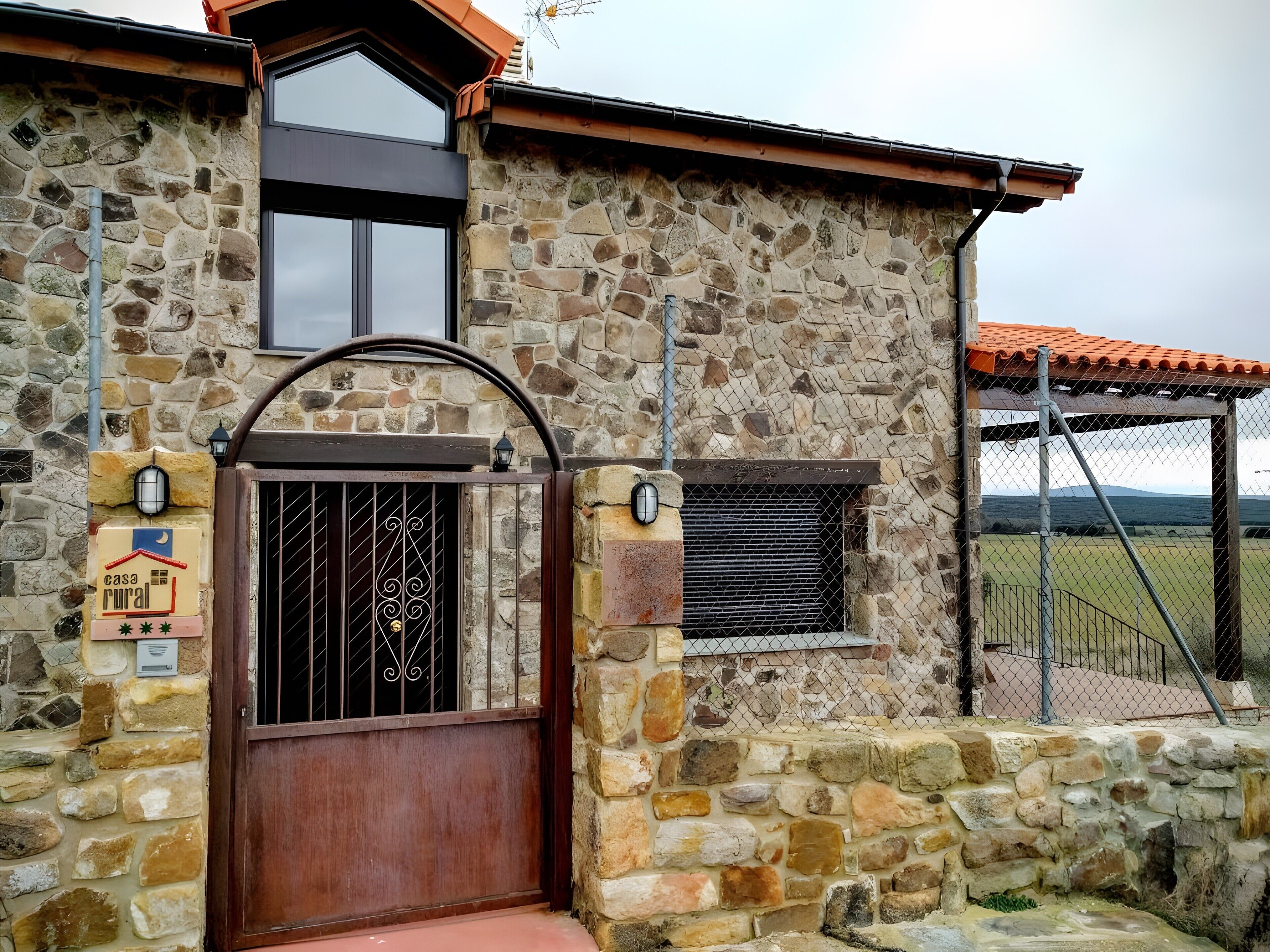 Edifici de pedra rústic amb una reixa metàl·lica, una petita finestra i un senyal que indica una casa rural.