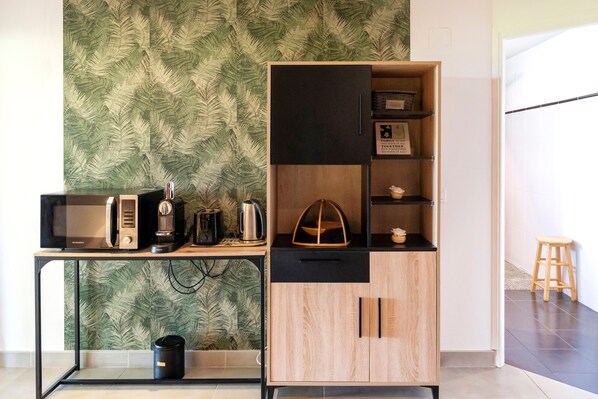 Una kitchenette equipada con microondas, tostadora, hervidor y un mueble de madera con puerta negra.