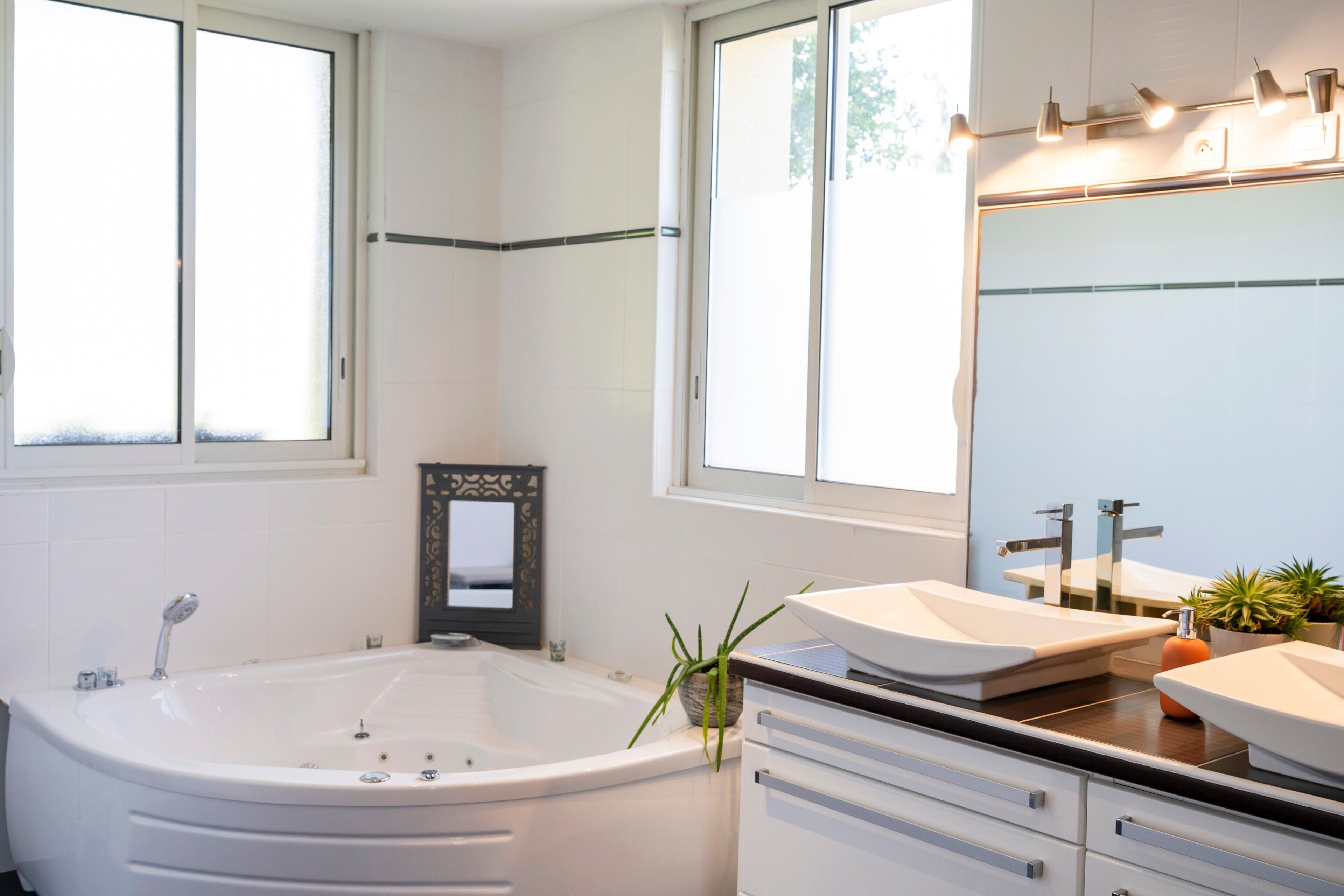 A modern bathroom with a bathtub, two sinks, a mirror, and a window.