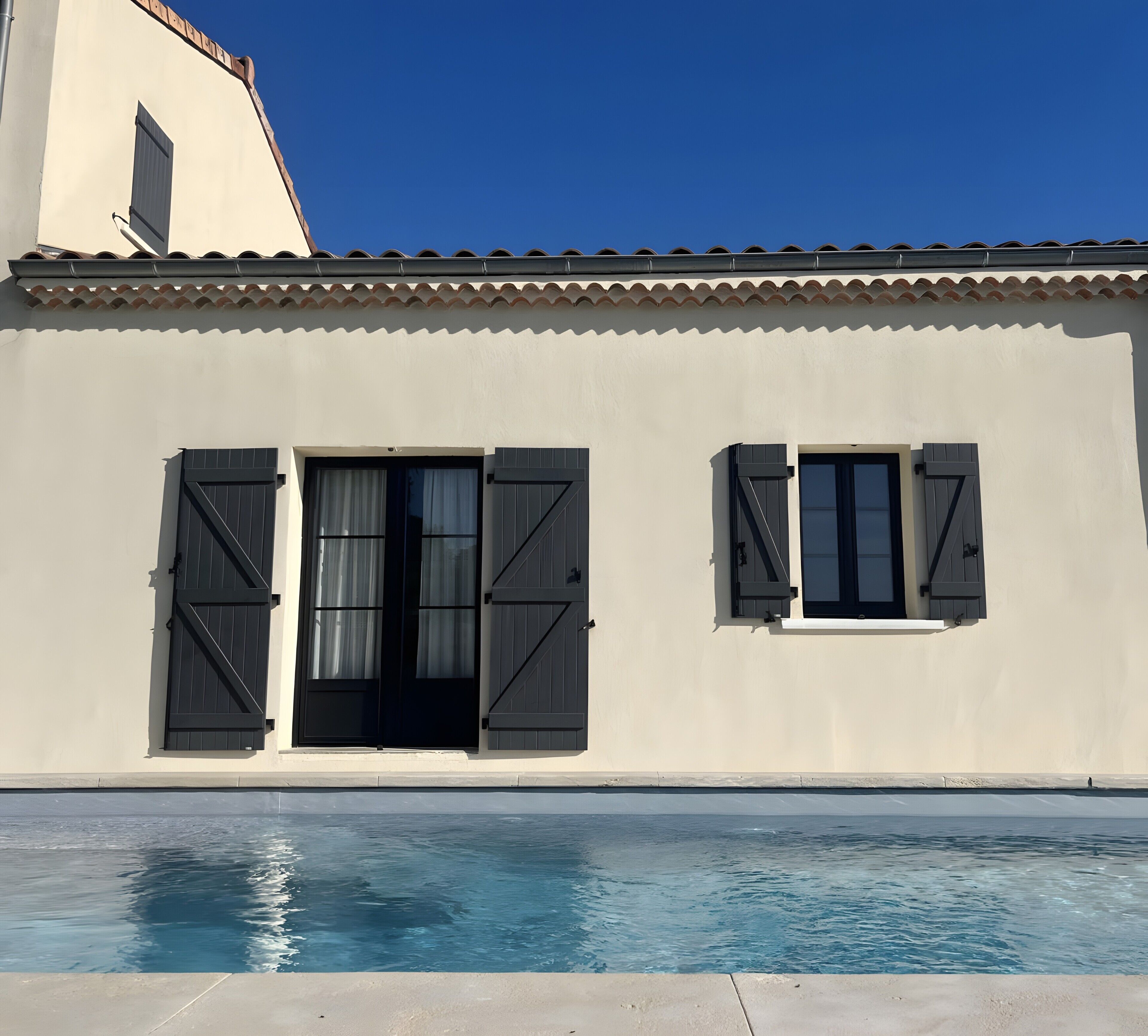 Ein Gebäude mit Schwimmbecken, zwei Fenstern mit Fensterläden und einem Ziegeldach.