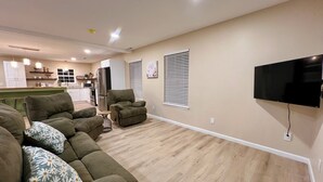 Una sala de estar con un sofá modular, un sillón reclinable y un televisor de pantalla plana montado en la pared.