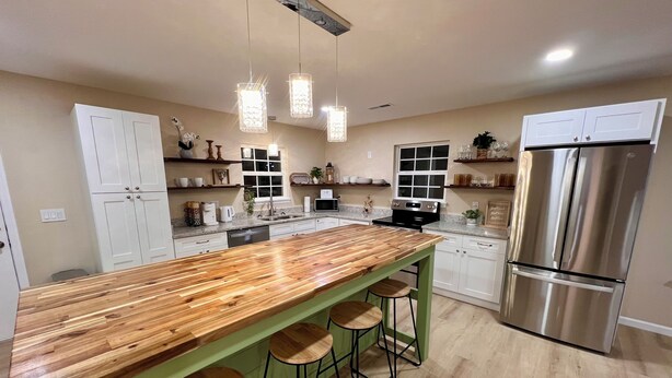 Cocina moderna con una isla de madera, taburetes de bar, electrodomésticos de acero inoxidable e iluminación colgante.