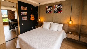 Quarto com cama, um violão, obras de arte e vista para o exterior.