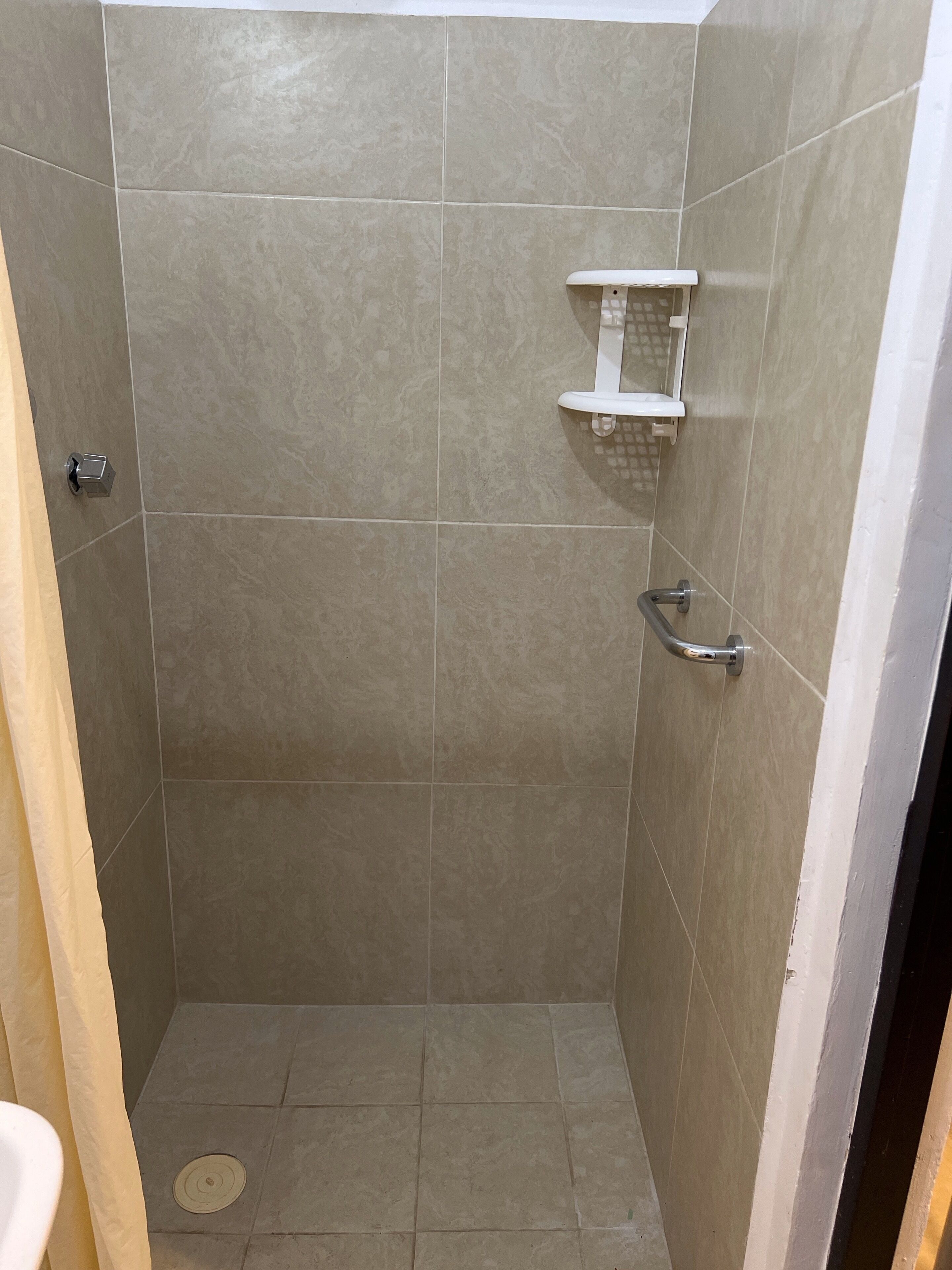 A small, tiled shower stall with a white shelf and a handrail.