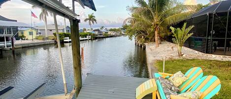 A dock with a covered seating area and a view of a calm waterway with boats.