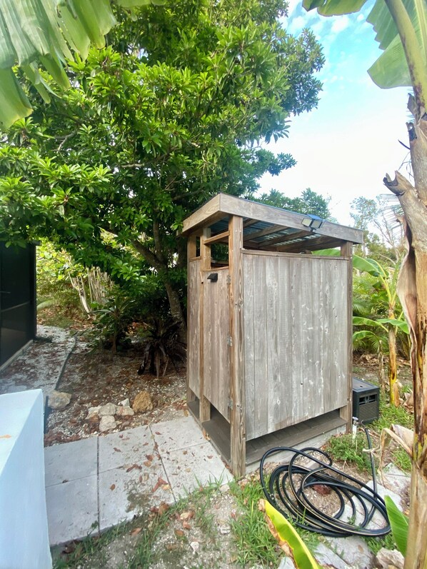 A wooden shed with a slanted roof, surrounded by lush greenery and a tree.
