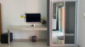 A hotel room with a flat-screen TV mounted on the wall, a small trash bin, and a sliding glass door leading to a hallway. - Tonsom Residence (Uttaradit)